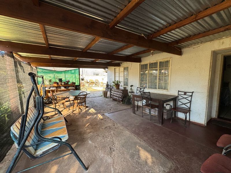 A covered outdoor patio area featuring a corrugated metal roof with exposed timber rafters and concrete flooring, providing a functional space for outdoor living.