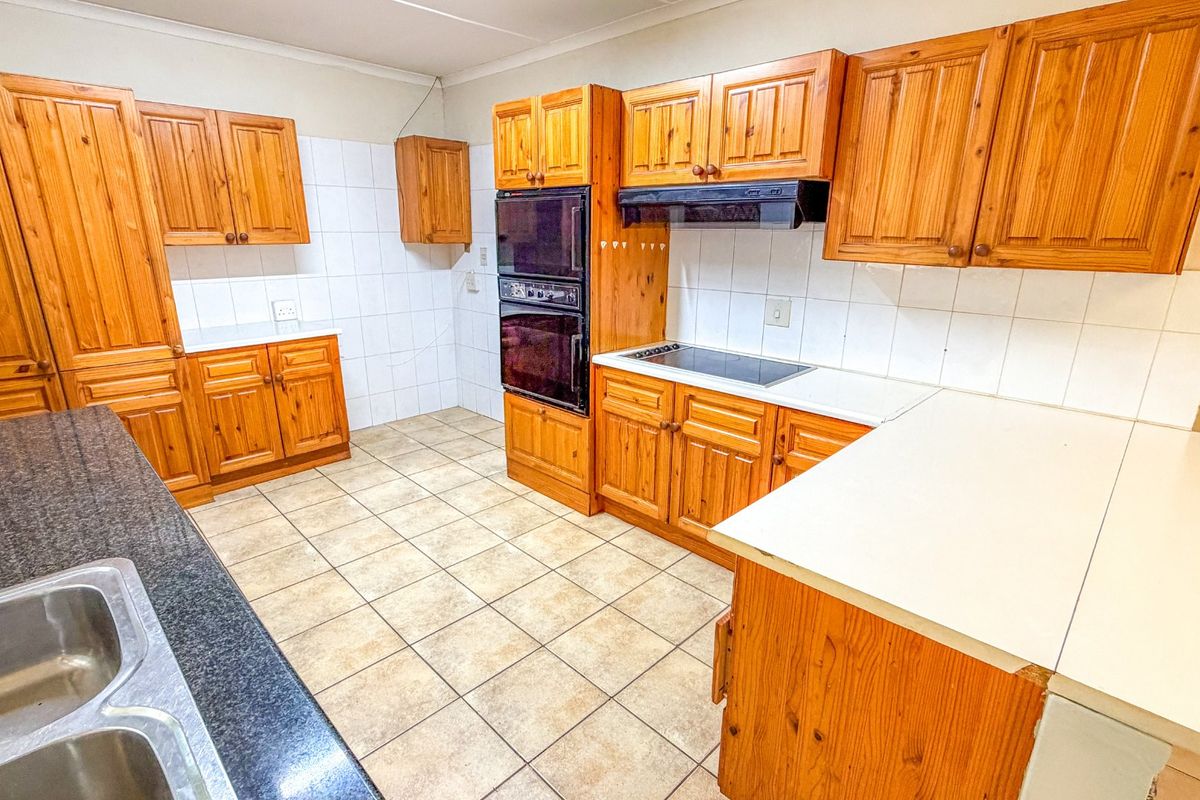 A functional kitchen featuring extensive wooden cabinetry, built-in double oven, electric hob, and tiled splashbacks, offering a classic layout ready for modernization.