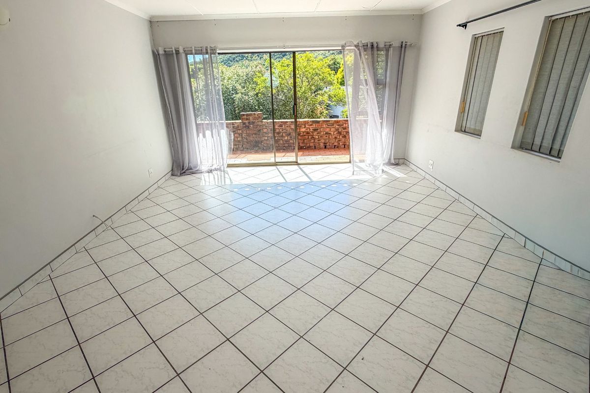 An empty living room featuring white tiled flooring and a large sliding glass door providing access to an outdoor balcony area.