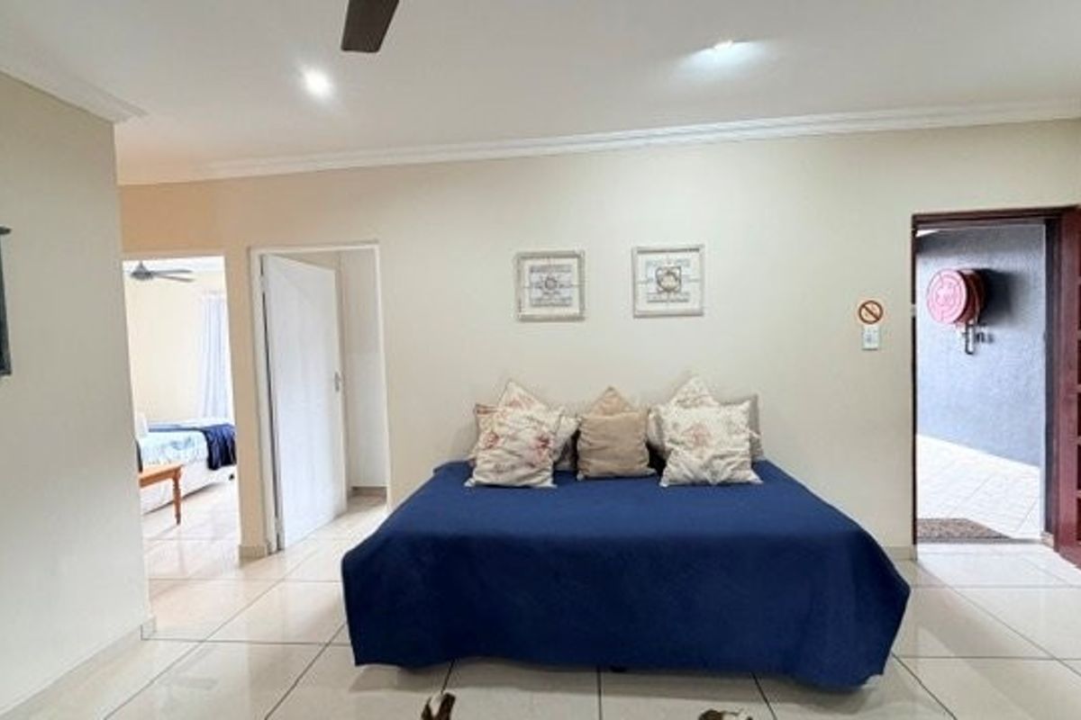 A spacious bedroom featuring tiled flooring, recessed lighting, and a ceiling fan, with direct access to an adjacent room and an exterior area.