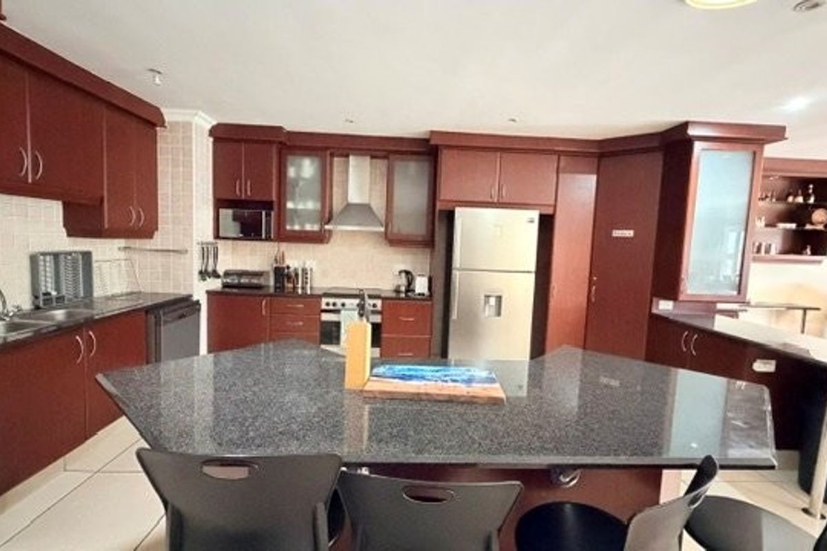 A spacious kitchen featuring dark wood cabinetry, granite countertops, a central breakfast bar, and integrated appliances, offering a functional layout for cooking and dining.