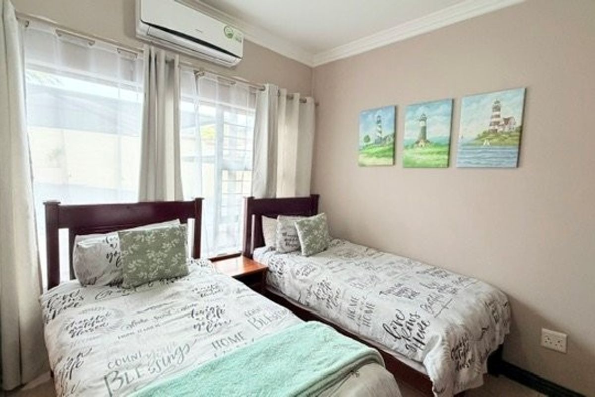 A well-maintained bedroom featuring a split-system air conditioner, neutral wall tones, and large windows allowing for natural light.