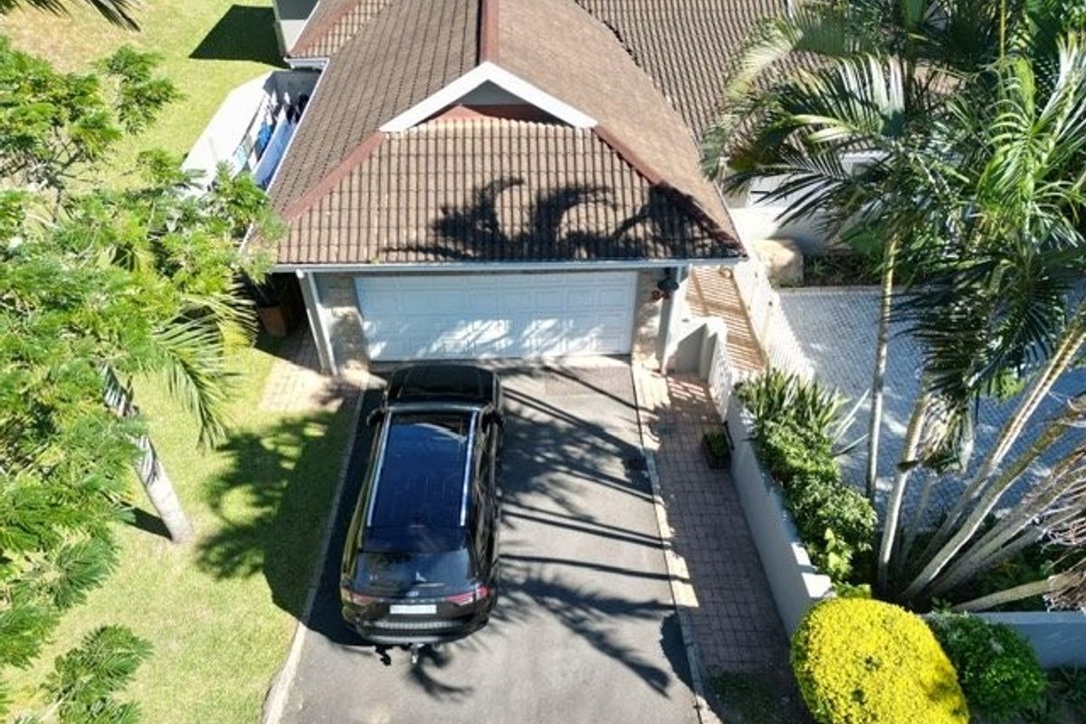 Aerial view of the townhouse property featuring a tiled roof, double garage, paved driveway, and established garden surroundings.