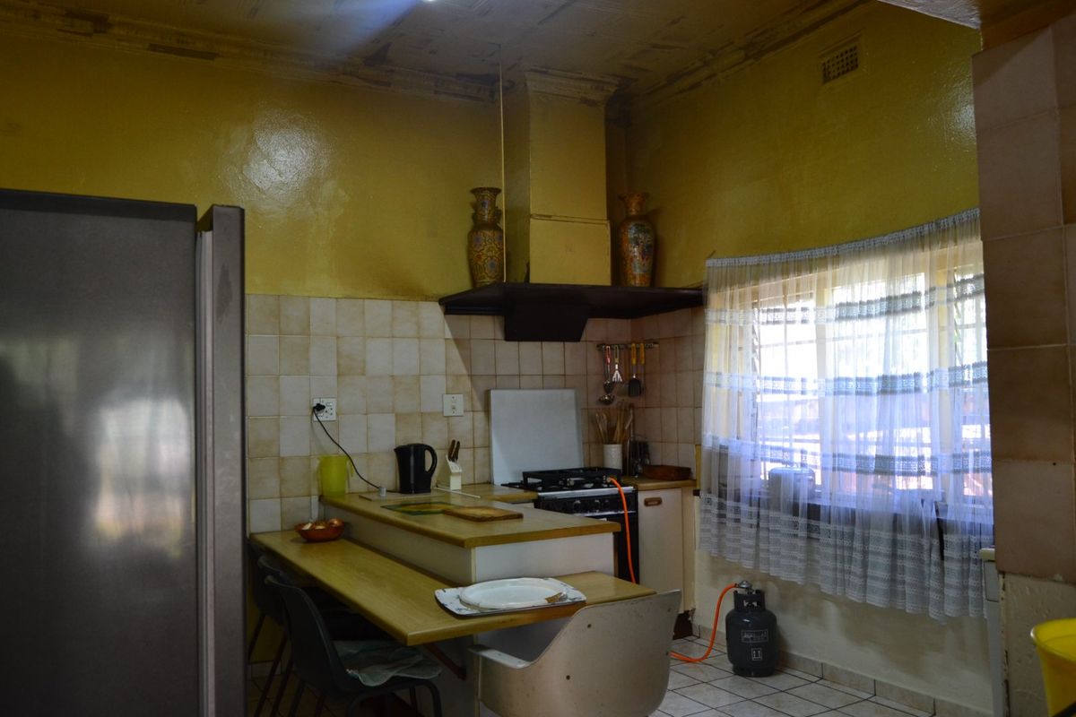 A dated kitchen featuring a gas stove, extractor fan, tiled backsplash, and a built-in breakfast counter, requiring cosmetic updates and ceiling repairs.