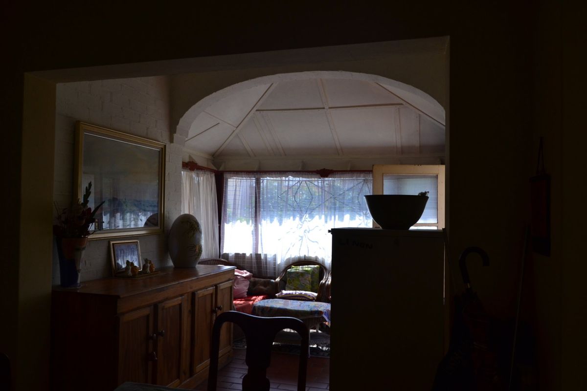 A living area featuring an arched transition to a sunroom with a vaulted ceiling, exposed brick walls, and tiled flooring.