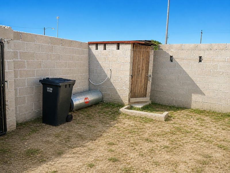 An outdoor utility area featuring a small block-built structure with a wooden door, enclosed by cinder block boundary walls.