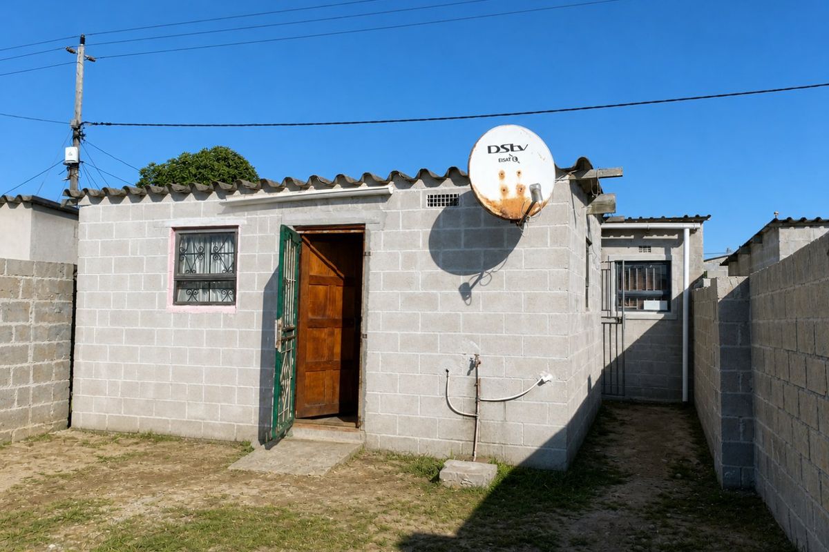 Rear view of a concrete block house featuring a security gate, timber door, and perimeter boundary walls in a compact yard setting.
