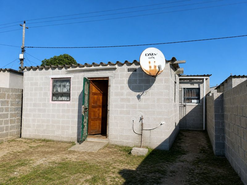 Rear view of a concrete block house featuring a security gate, timber door, and perimeter boundary walls in a compact yard setting.