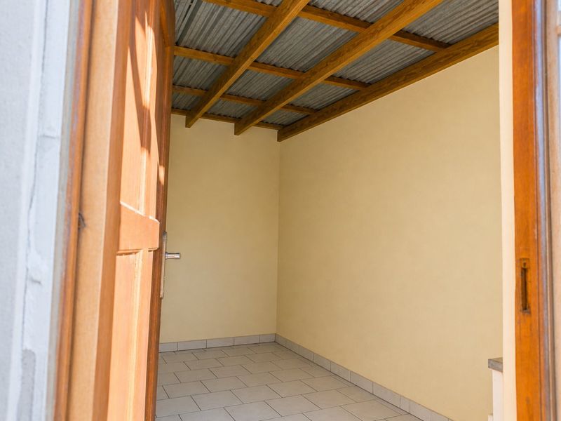 A covered outdoor patio area featuring tiled flooring, exposed timber roof beams, and a corrugated metal ceiling.