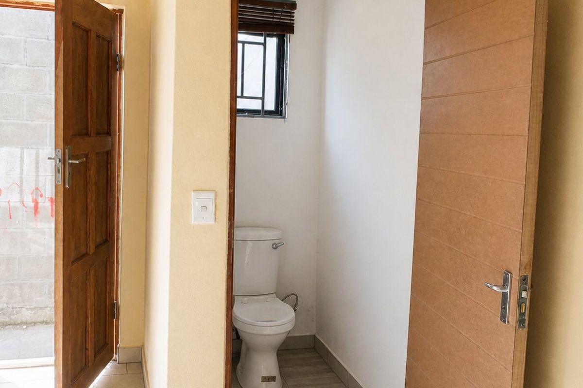 A functional bathroom space featuring a toilet, tiled flooring, and direct access to an outdoor area through an adjacent doorway.