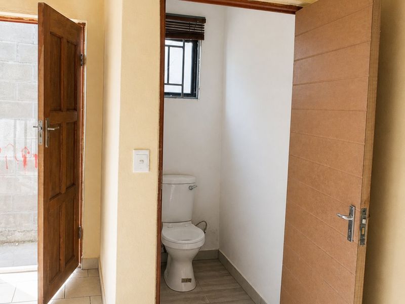 A functional bathroom space featuring a toilet, tiled flooring, and direct access to an outdoor area through an adjacent doorway.