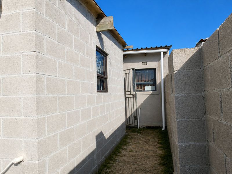 A narrow side passage between concrete block structures featuring security gates and aluminium window frames.