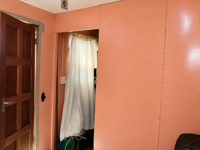 A hallway area featuring peach-colored wall panels, a wooden door, and tiled flooring, currently showing signs of unfinished construction and visible panel seams.