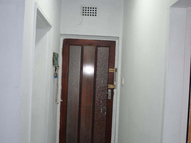 A functional hallway featuring tiled flooring, a timber door with glass inserts, and a ceiling light fixture.