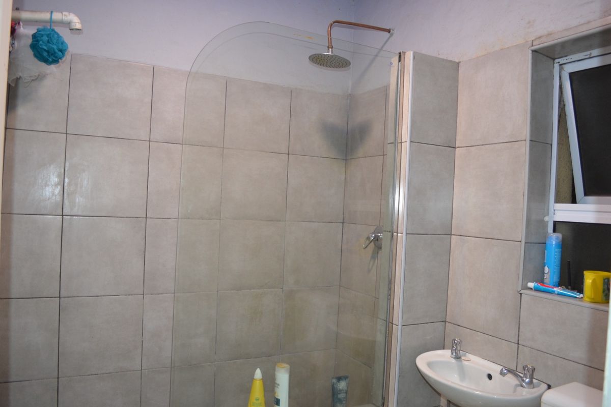 A bathroom featuring a shower with a glass screen, wall tiling, and a small basin. The space requires maintenance and updates to improve its condition.