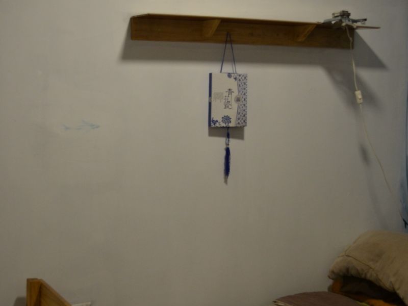A bedroom featuring a wall-mounted wooden shelf and standard electrical fixtures, requiring cosmetic updates to the wall surfaces.