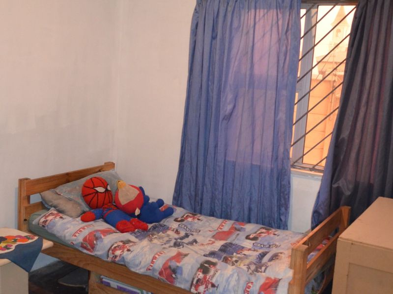 A bedroom featuring parquet flooring, a window with security bars, and an air vent. The space requires cosmetic updates to the wall finishes.