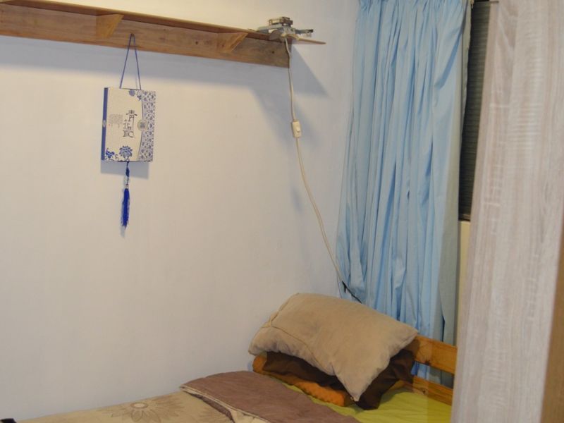 A compact bedroom featuring a wall-mounted wooden shelf and window with curtains.