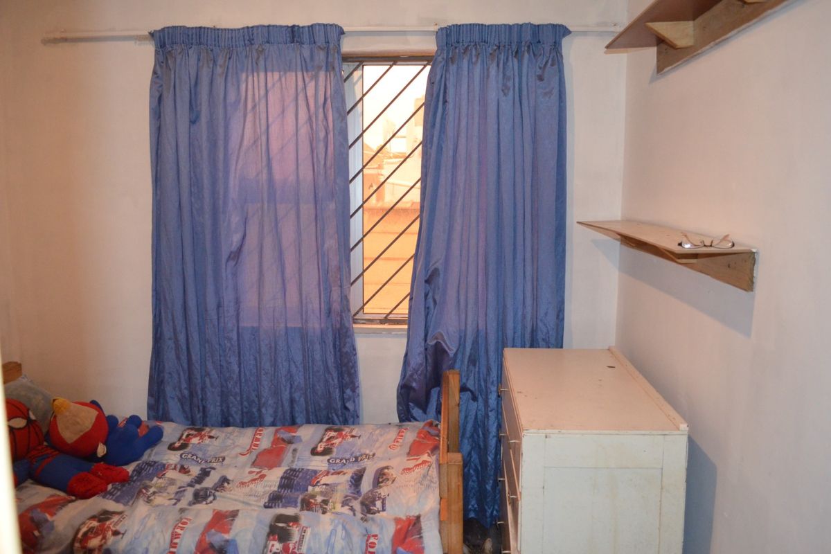 A bedroom featuring a window with security bars and wall-mounted shelving units.