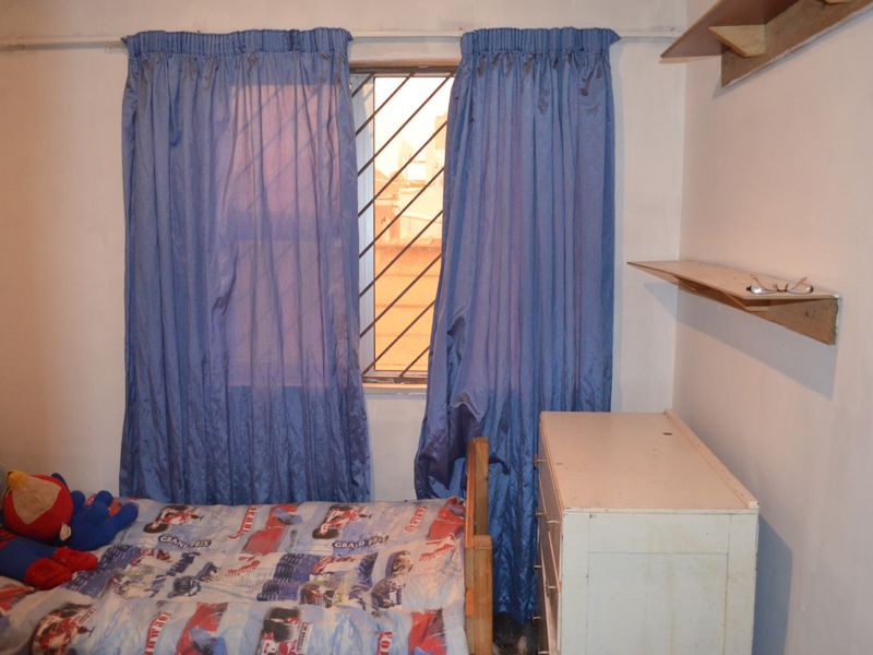 A bedroom featuring a window with security bars and wall-mounted shelving units.