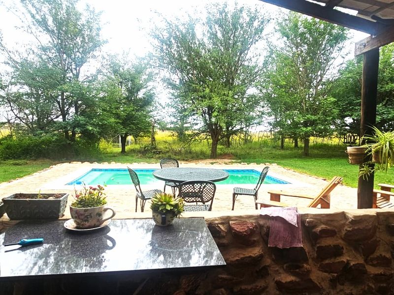 A covered patio area featuring rustic stone walling and timber supports, overlooking a private swimming pool and lush garden landscape.