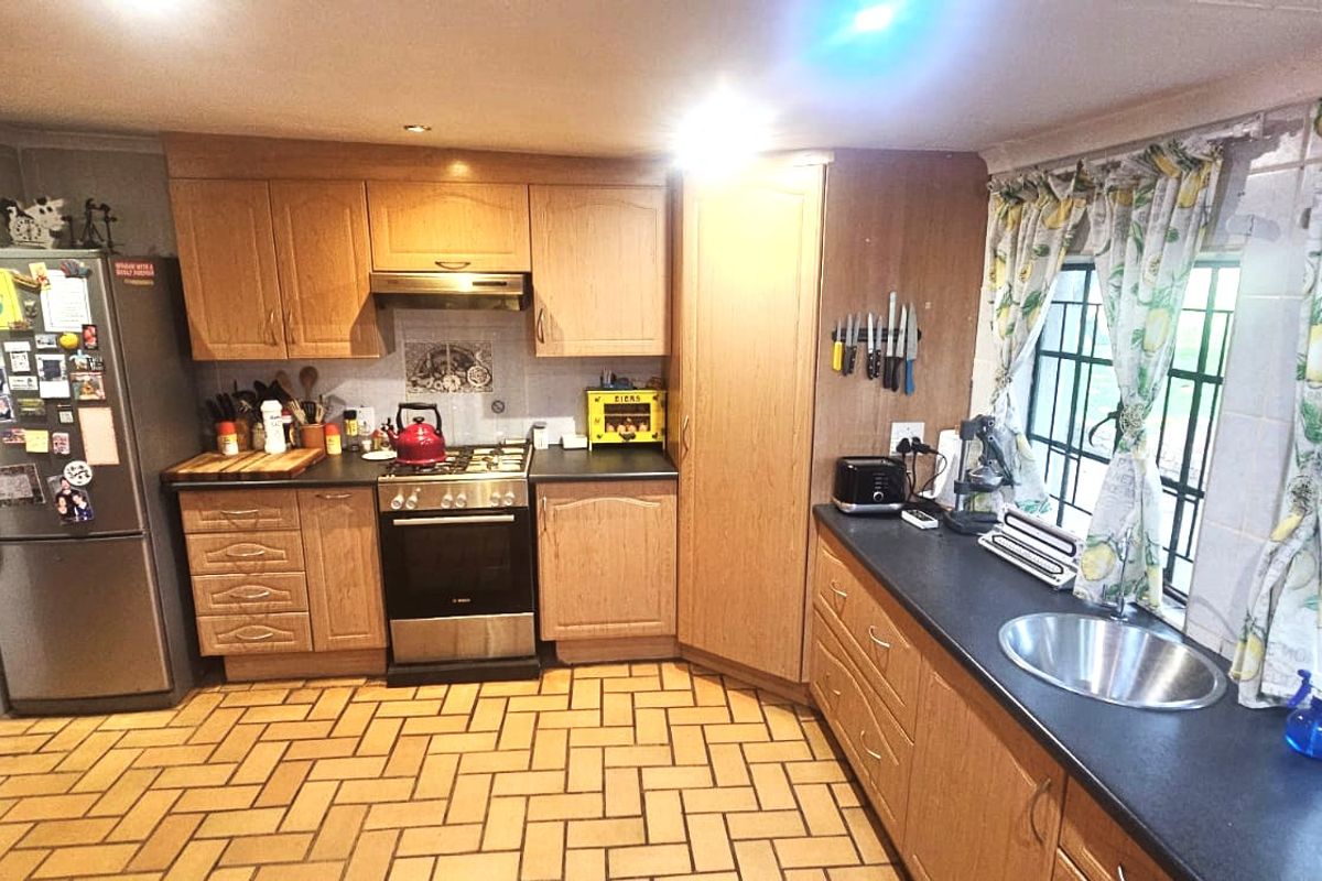 A functional kitchen featuring wooden cabinetry, laminate countertops, a gas hob with extractor fan, and tiled flooring with security-barred windows.