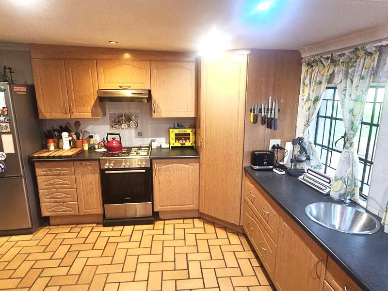 A functional kitchen featuring wooden cabinetry, laminate countertops, a gas hob with extractor fan, and tiled flooring with security-barred windows.