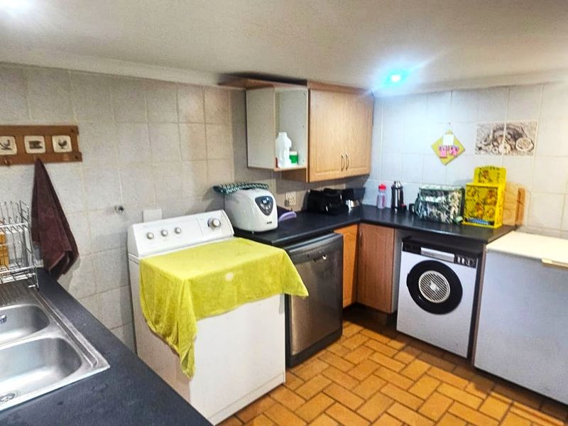 Functional laundry area featuring a double basin stainless steel sink, tiled splashbacks, and ample built-in cabinetry with durable tiled flooring.