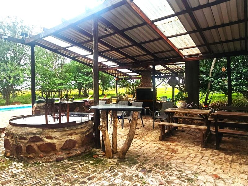 A rustic covered outdoor patio area featuring a built-in braai, stone masonry, and brick paving, ideal for farm-style outdoor entertaining.
