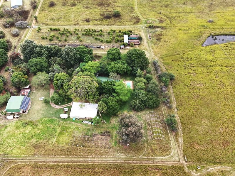 Aerial view of a farm property featuring multiple outbuildings, a swimming pool, solar panels, an orchard, and a small dam set within open pasture.