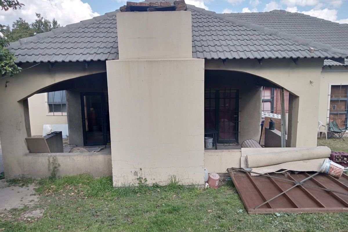 Covered patio area featuring a prominent masonry chimney, arched architectural details, and tiled roofing, currently requiring maintenance and exterior finish repairs.
