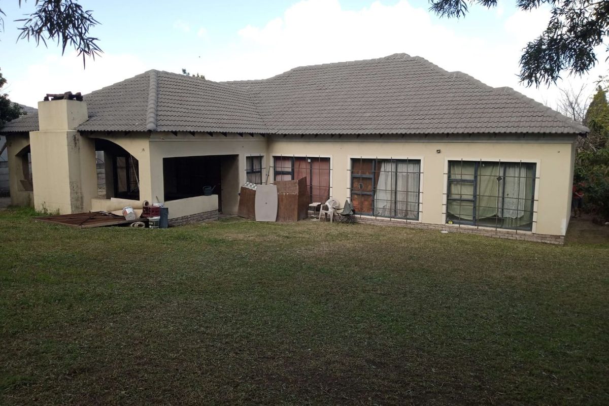 Rear view of a single-story house featuring a tiled roof, covered patio area, and large sliding doors with security bars, set within a spacious garden.