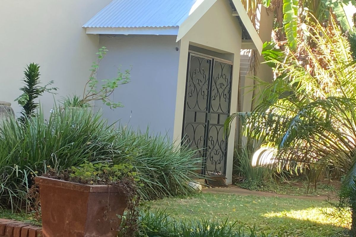 A small utility structure with a corrugated metal roof and decorative wrought iron security gate, situated in a landscaped garden setting.