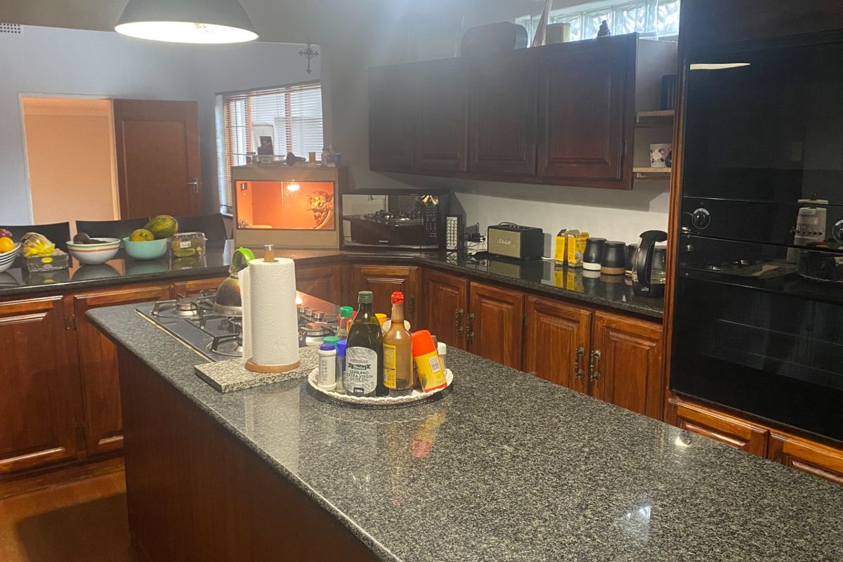 A functional kitchen featuring dark wooden cabinetry, granite countertops, a central island with a gas hob, and a built-in oven.