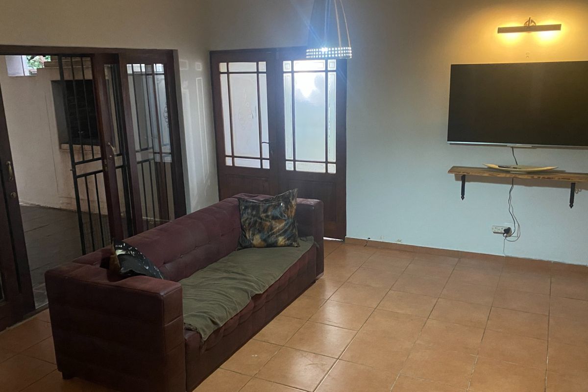 A living room featuring tiled flooring, timber-framed glass doors providing outdoor access, and wall-mounted shelving.