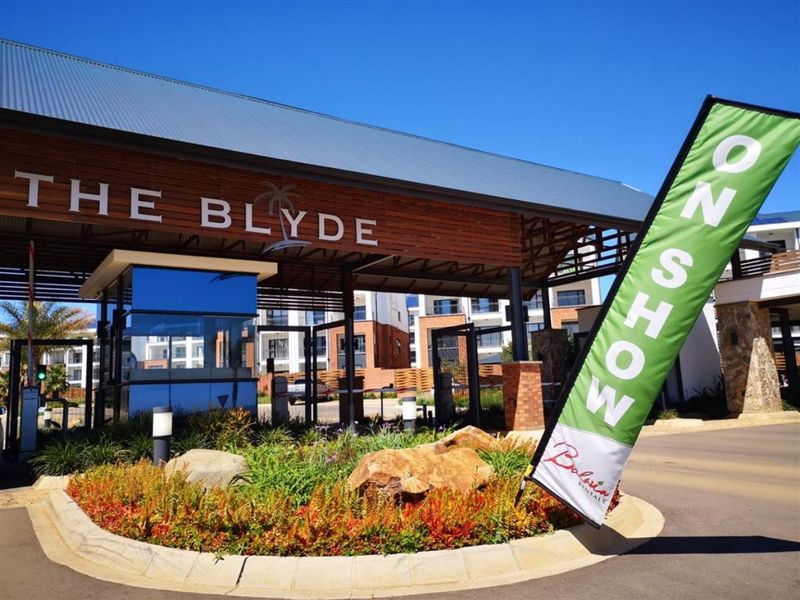 The main entrance and security gatehouse of The Blyde apartment complex, featuring modern architectural design and well-maintained landscaping.