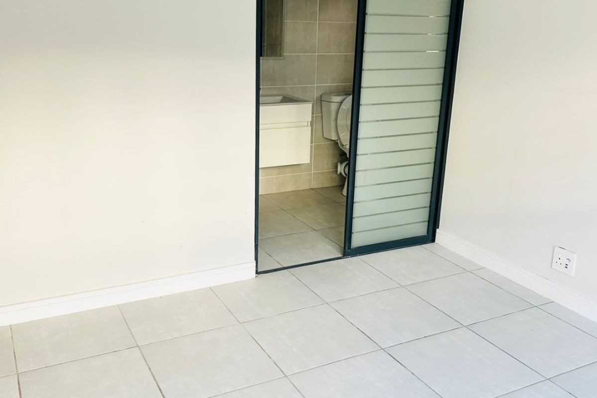 An empty bedroom featuring neutral tiled flooring and a modern sliding door providing access to an en-suite bathroom.