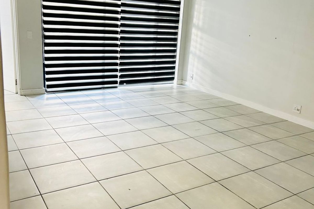 A bright, empty living room featuring neutral tiled flooring, a large sliding glass door with modern zebra blinds, and clean white walls.