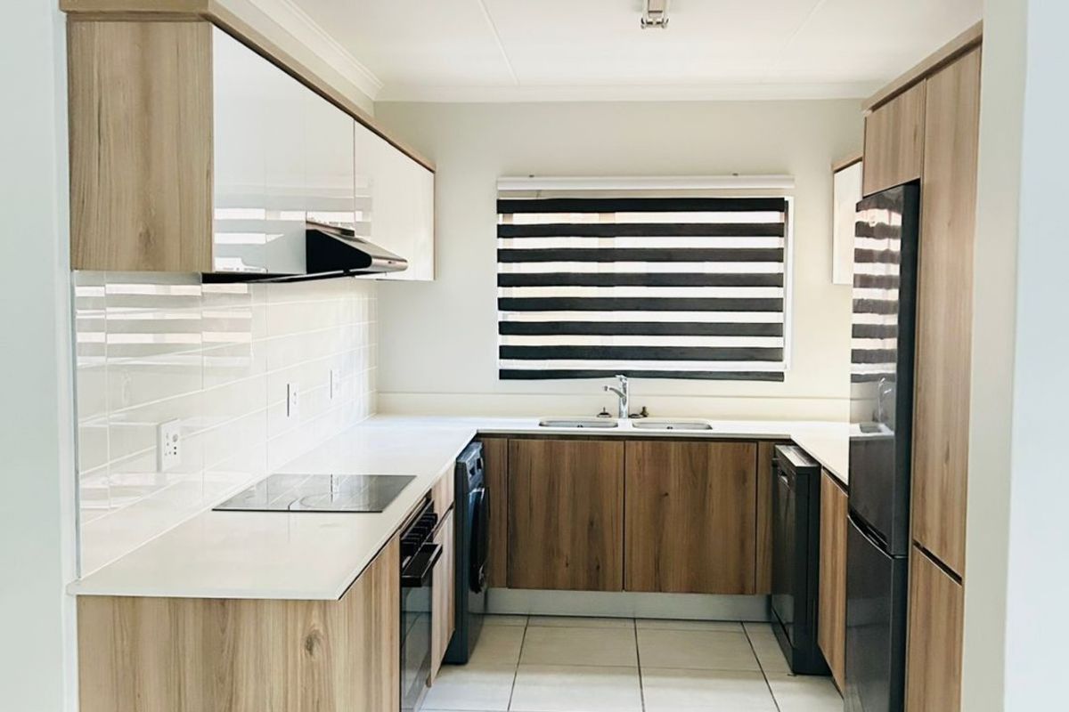 Modern, well-maintained kitchen featuring wood-finish cabinetry, stone countertops, tiled flooring, and integrated appliances in a clean, functional layout.