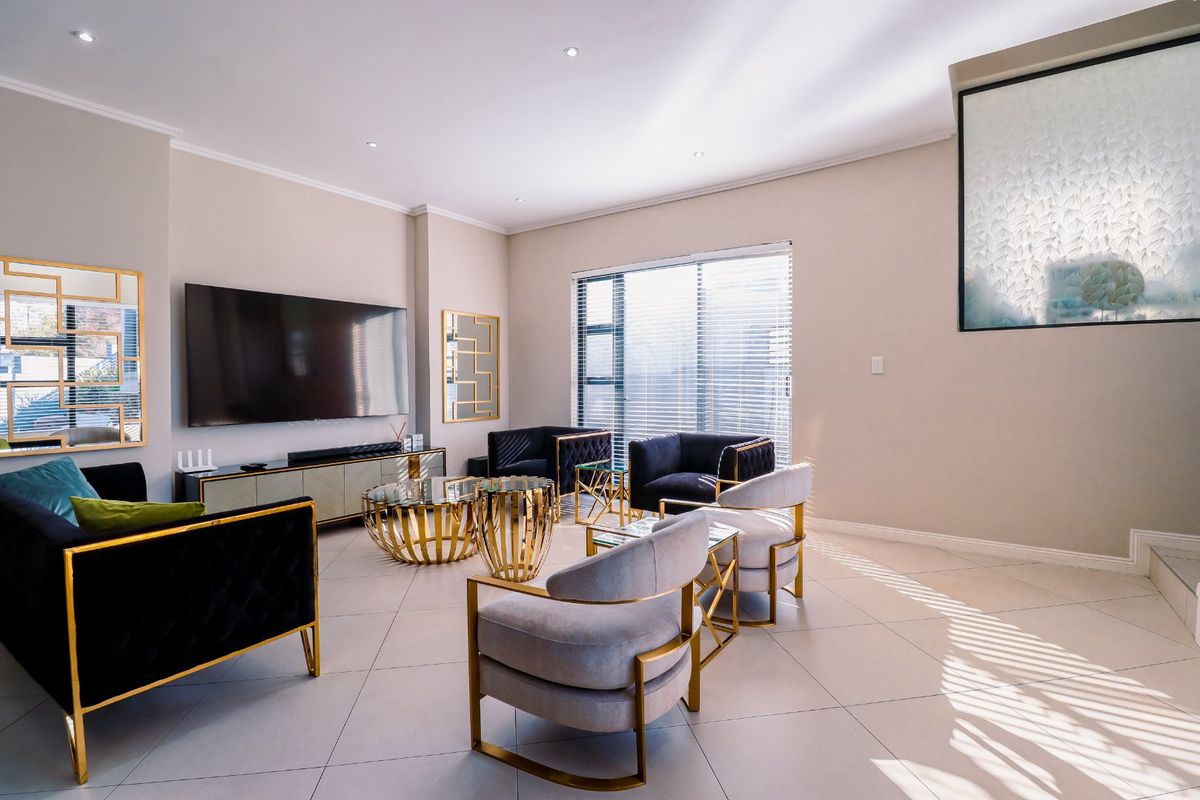 A bright and modern living room featuring large format floor tiles, recessed downlighting, and a large window with fitted blinds.