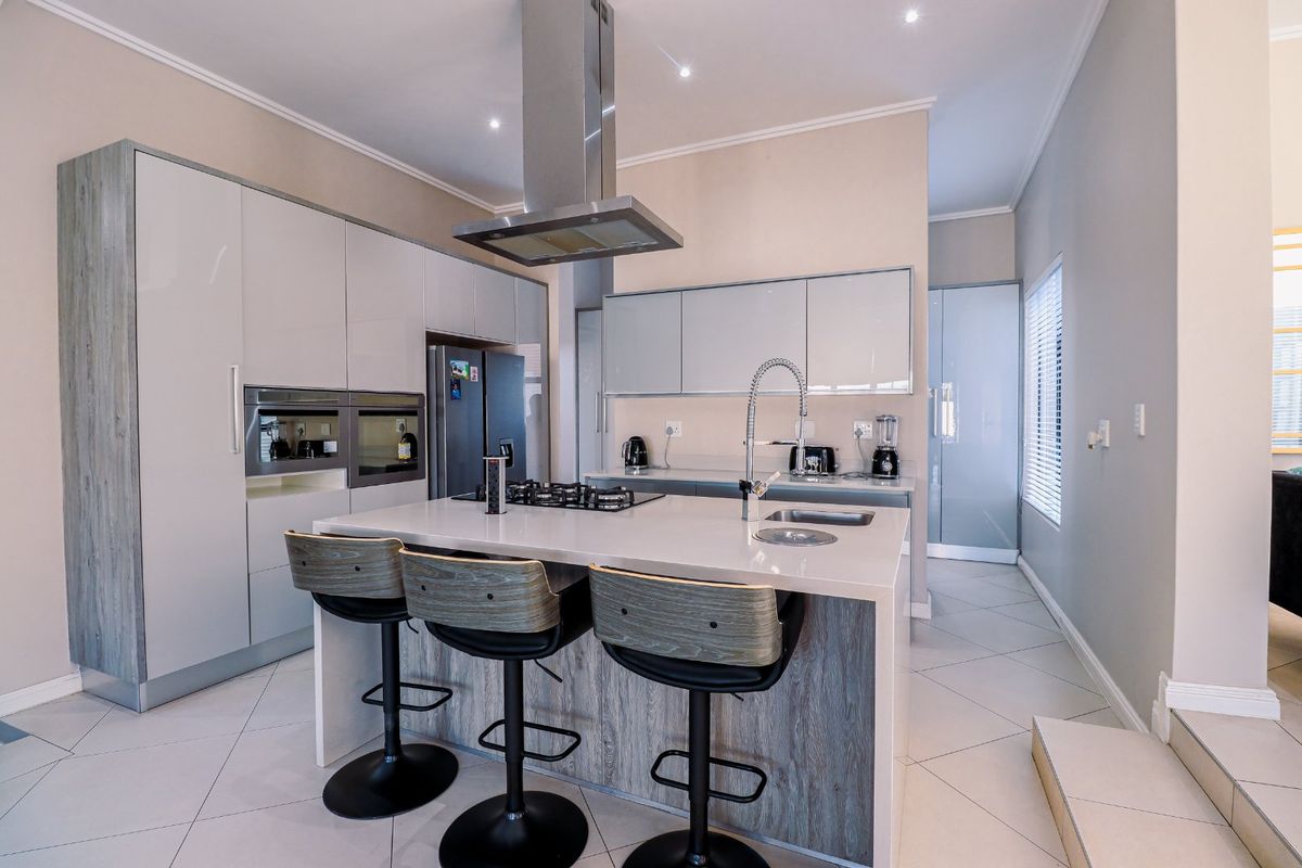 Modern kitchen featuring a central island with a built-in gas hob, stainless steel extractor fan, sleek cabinetry, and integrated appliances.