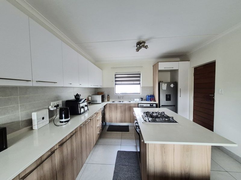Modern kitchen featuring wood-finish lower cabinetry, white upper cabinets, stone countertops, a central island with a gas hob, and tiled flooring.