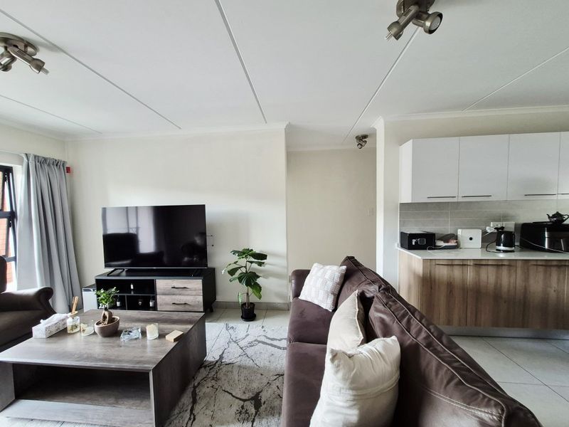 An open-plan living area featuring tiled floors, a modern kitchen with built-in cabinetry, stone countertops, and integrated track lighting.