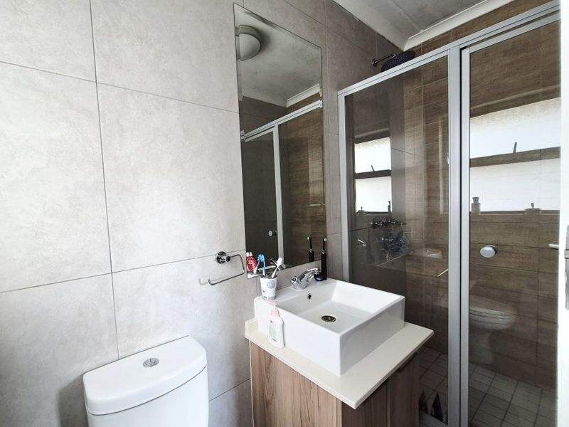 A compact bathroom featuring a modern vessel sink on a vanity cabinet, a glass-enclosed shower, and neutral wall tiling.