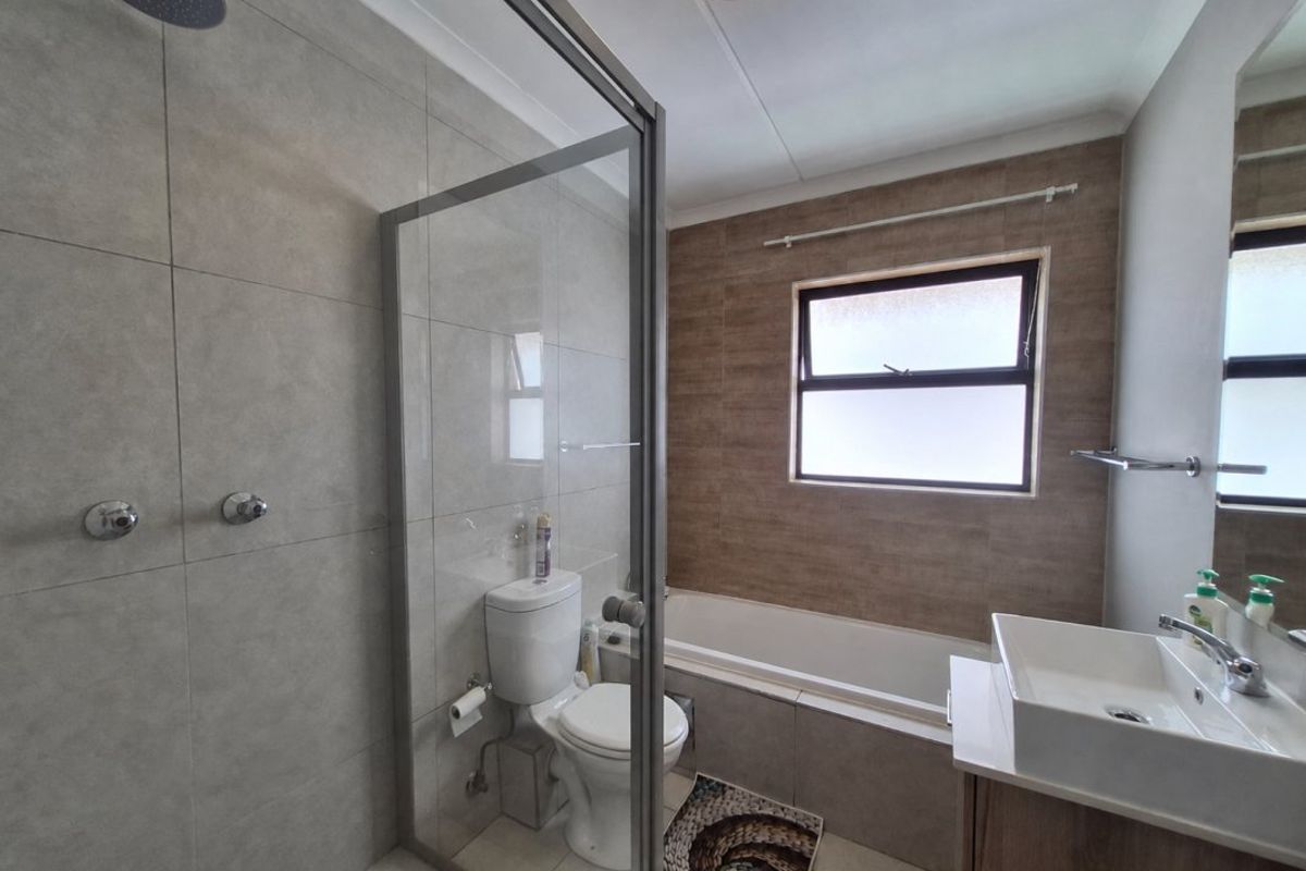 Modern bathroom featuring a walk-in shower with glass enclosure, a built-in bathtub, and a contemporary vanity basin with neutral wall tiling.