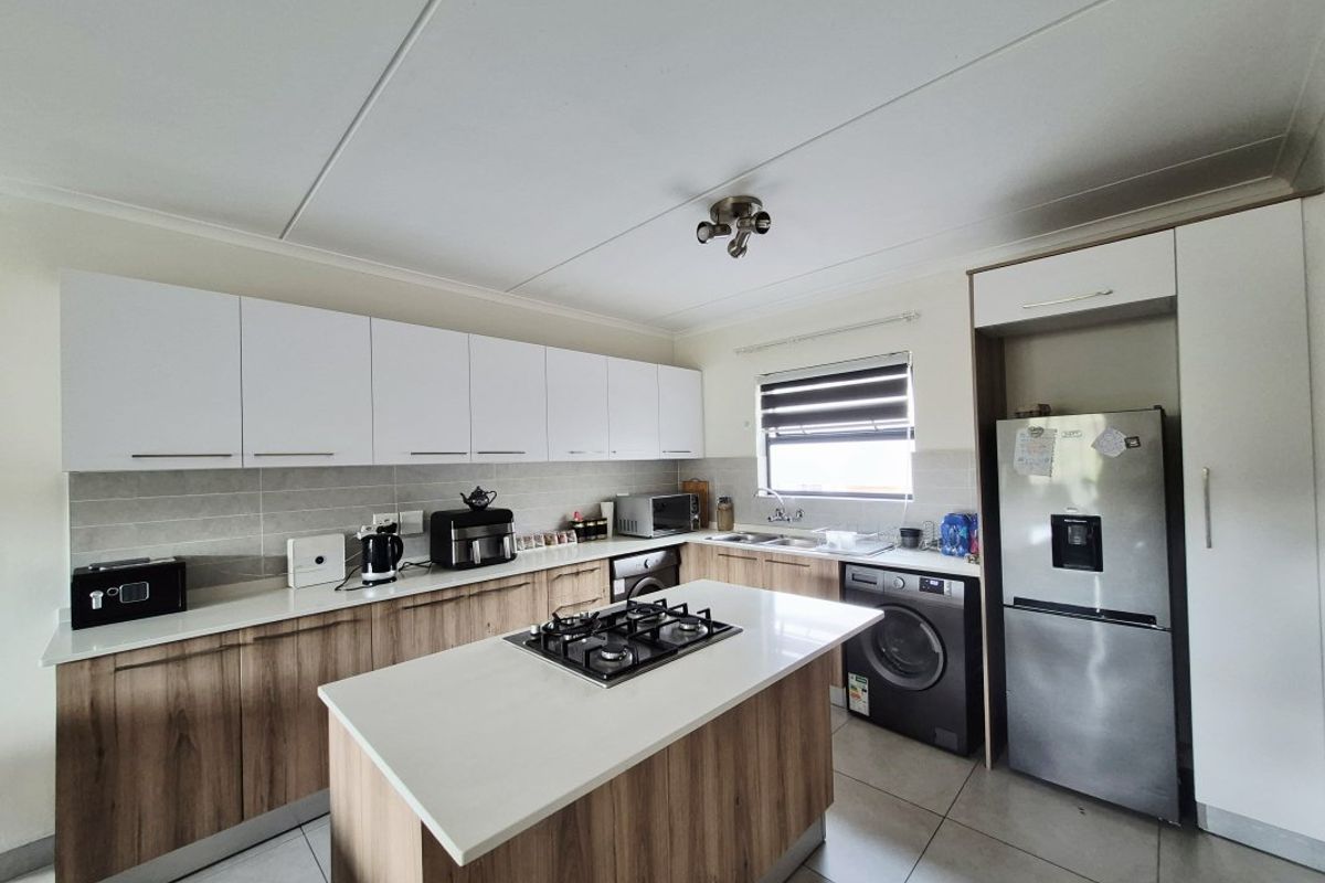 Modern kitchen featuring a central island with a gas hob, ample white and wood-grain cabinetry, stone countertops, and tiled flooring.
