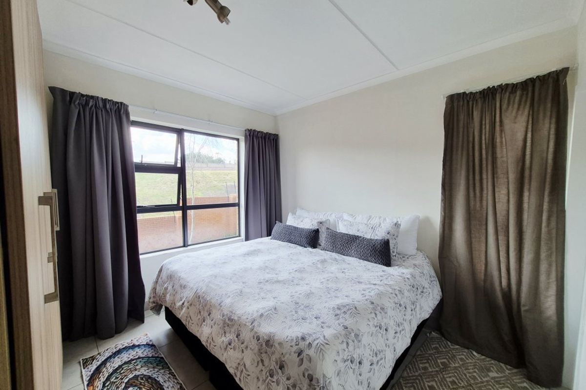 A well-maintained bedroom featuring tiled flooring, a built-in wardrobe, and an aluminium-framed window providing natural light.