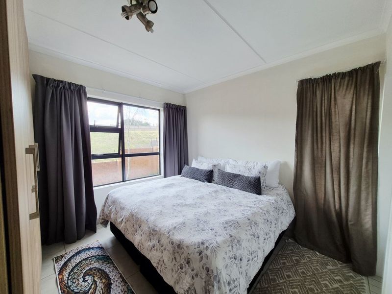 A well-maintained bedroom featuring tiled flooring, a built-in wardrobe, and an aluminium-framed window providing natural light.