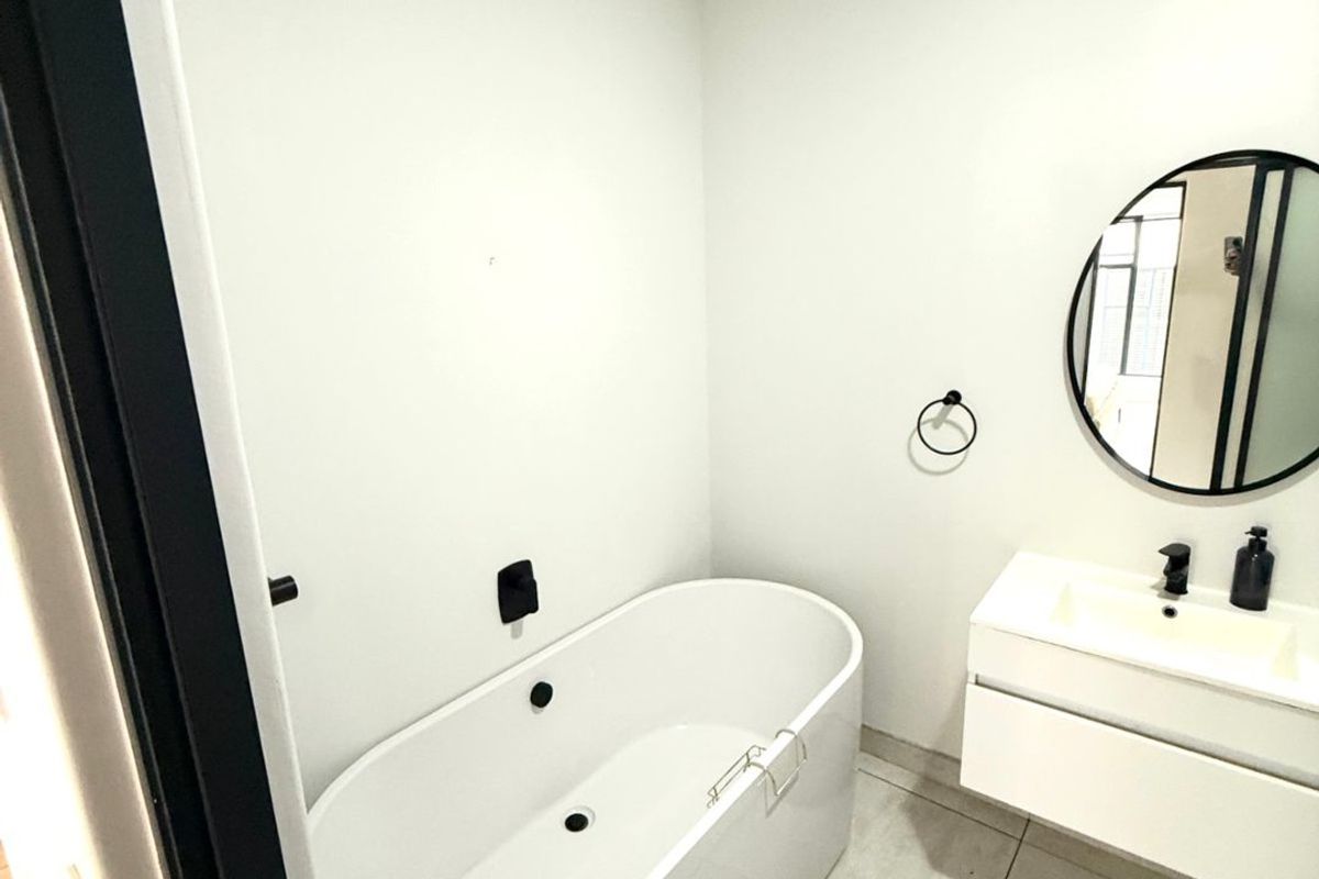Modern bathroom featuring a sleek freestanding bathtub, wall-mounted vanity with integrated basin, and contemporary black matte fixtures on tiled flooring.
