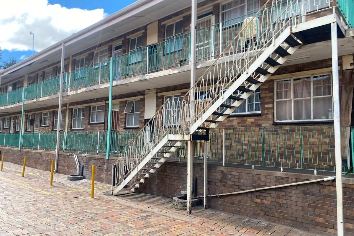 Exterior view of a multi-story apartment block featuring brick facade, external metal staircases, and balcony railings.